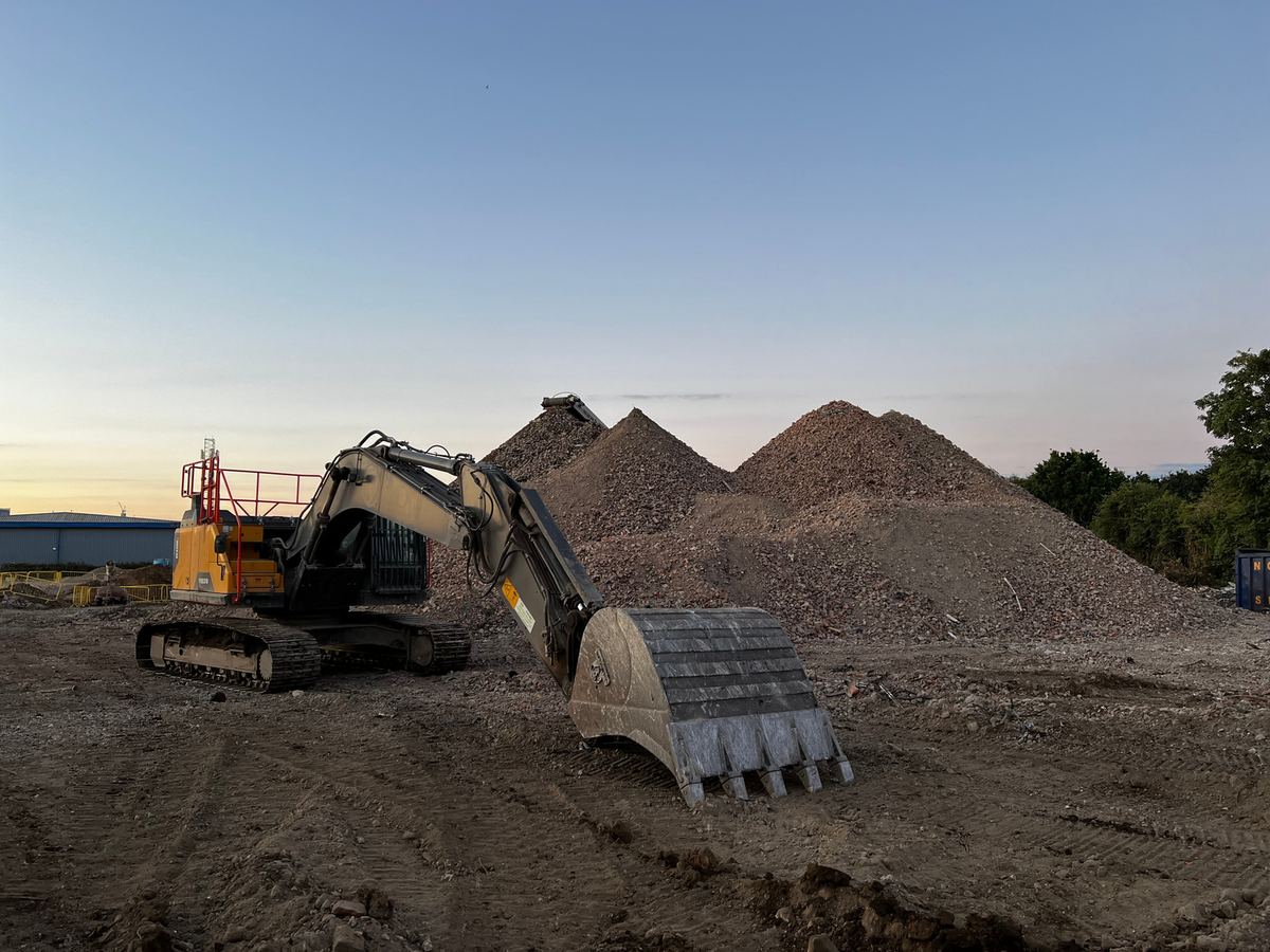 Excavator beside crushed aggregate stockpiles at sunset